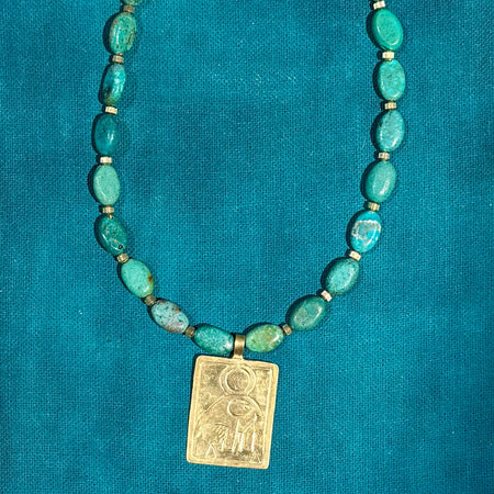 Necklace with turquoise beads and a gold pendant on a teal background